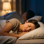 A woman asleep on her side by lamplight, her partner asleep behind her