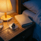 The open case of earplugs on a wooden nightstand beside a lamp, a book and a glass of water