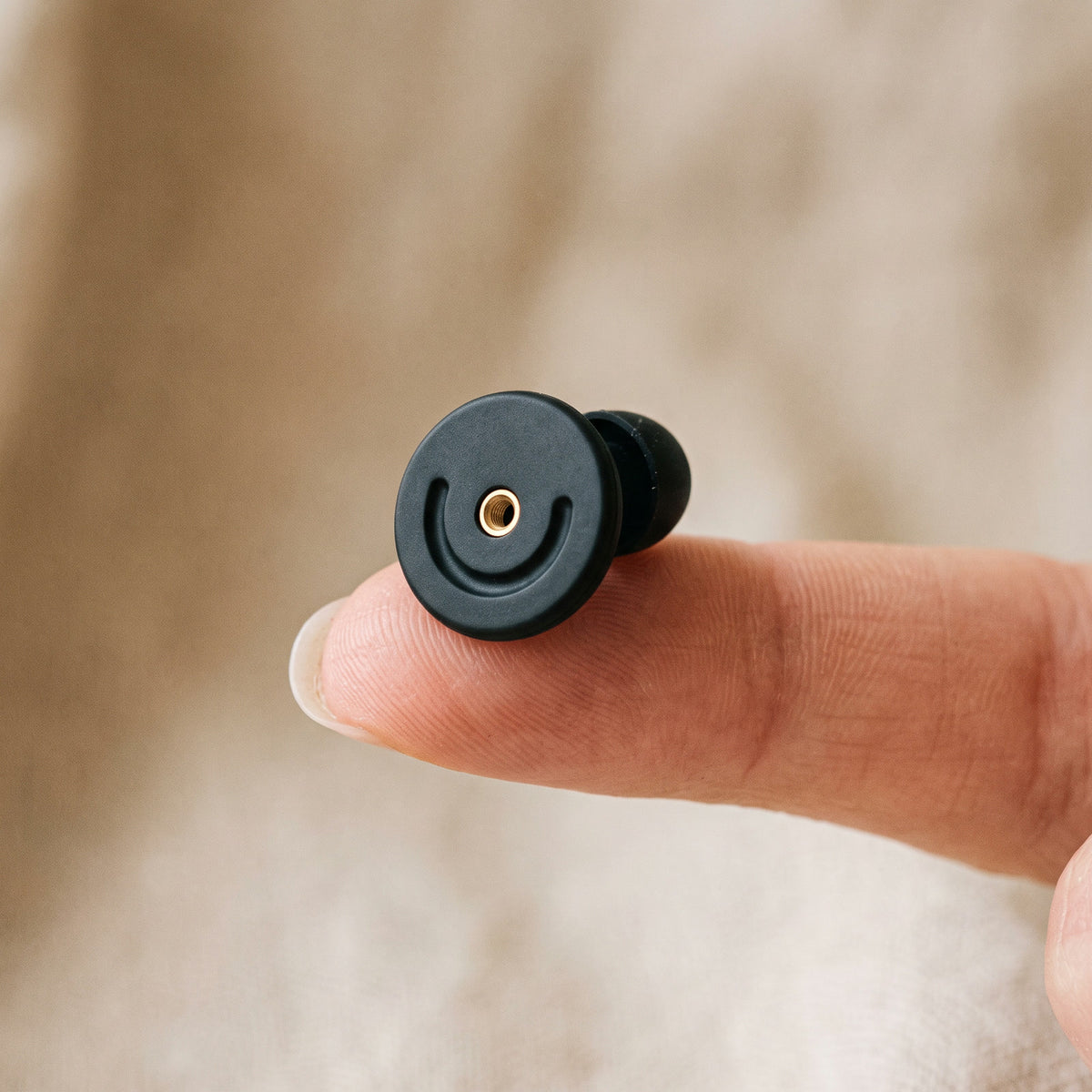 One round black silicone earplug resting on a fingertip