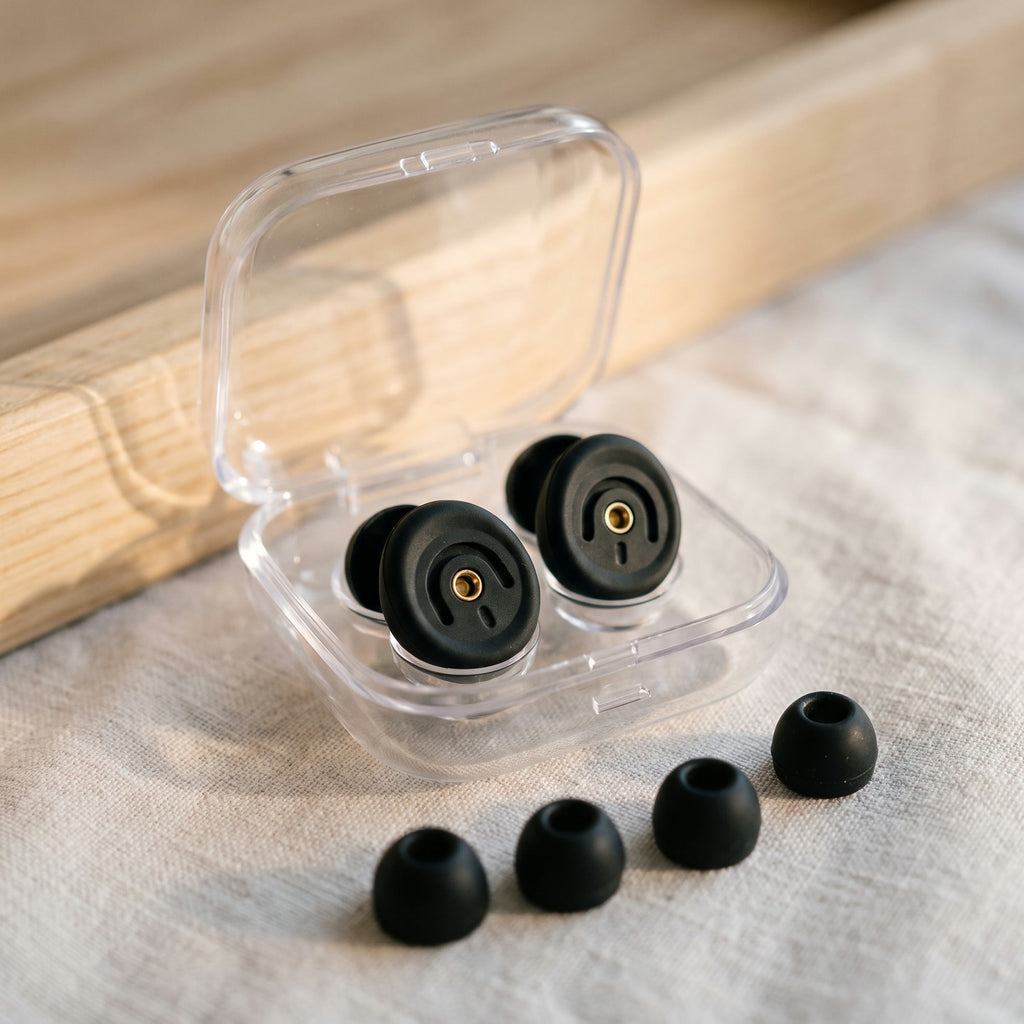 The clear case holding a pair of earplugs, with four ear tips on linen