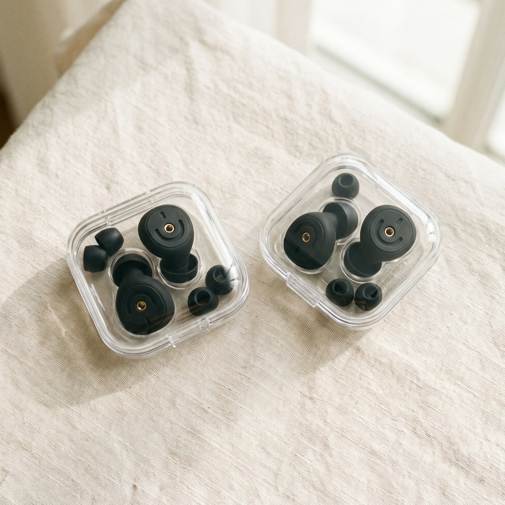 Two clear cases of earplugs and ear tips side by side on a white bed