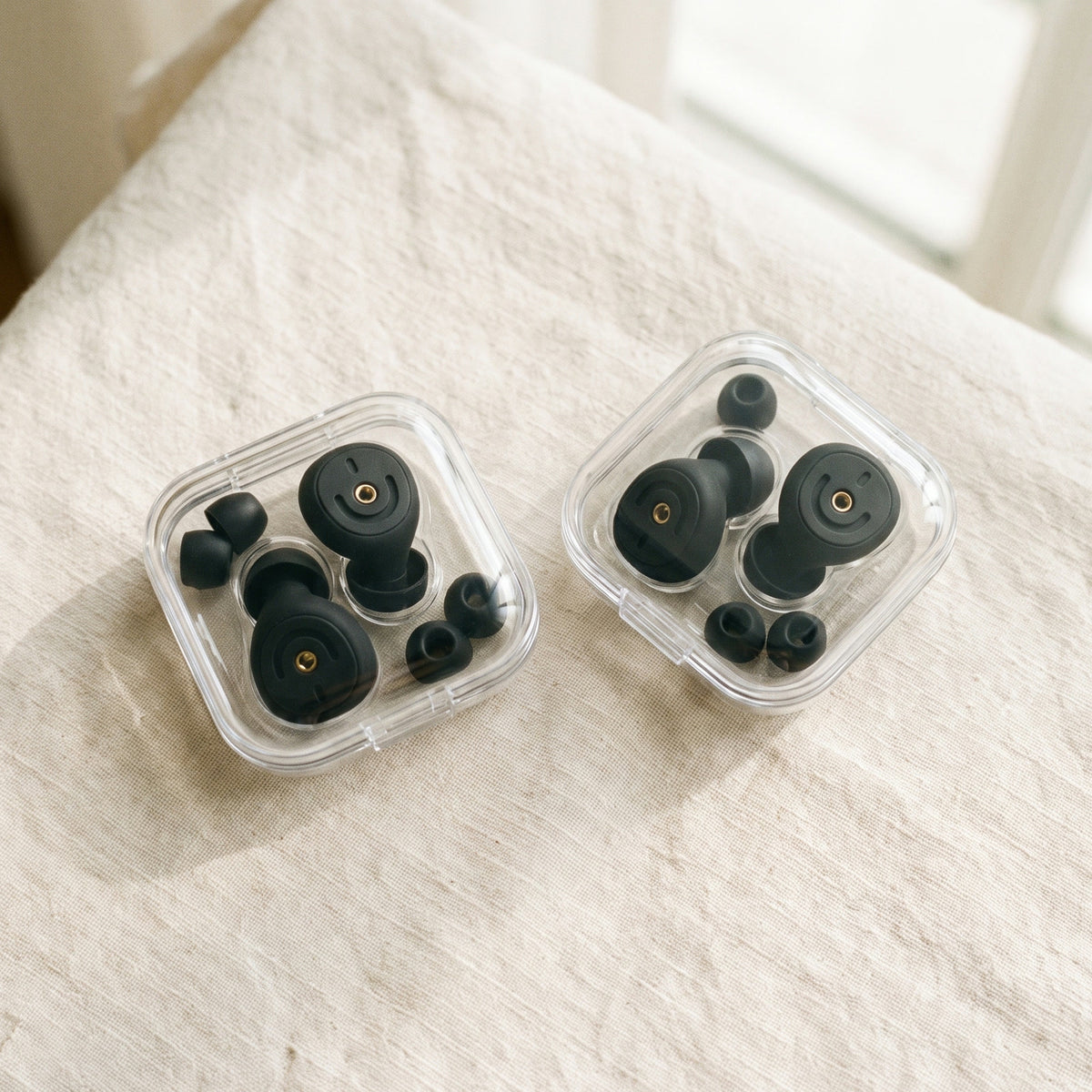 Two clear cases of earplugs and ear tips side by side on a white bed