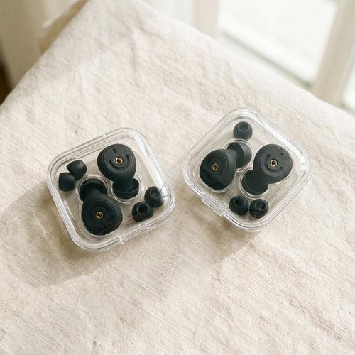 Two clear cases of earplugs and ear tips side by side on a white bed